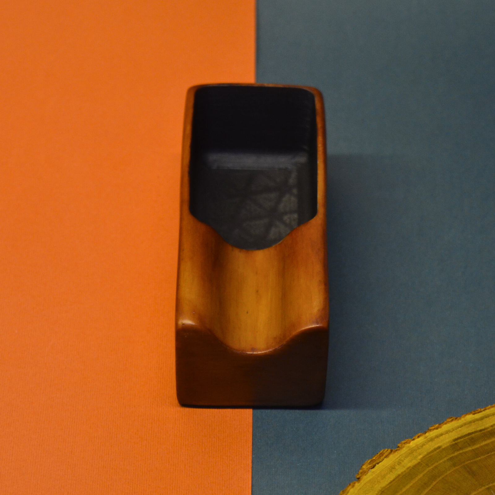 Wooden object with black interior on an orange and blue background