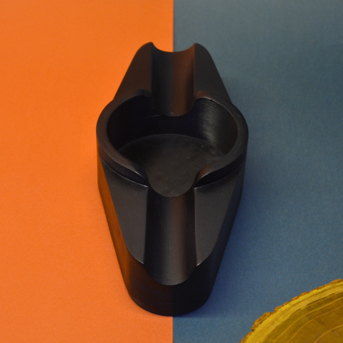Black ashtray object on a split orange and blue background