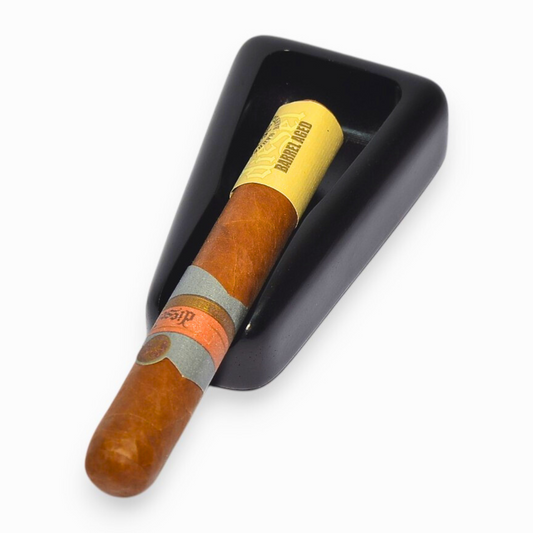 Cigar ashtray with a visible brand label resting on a black wedge-shaped object against a white background