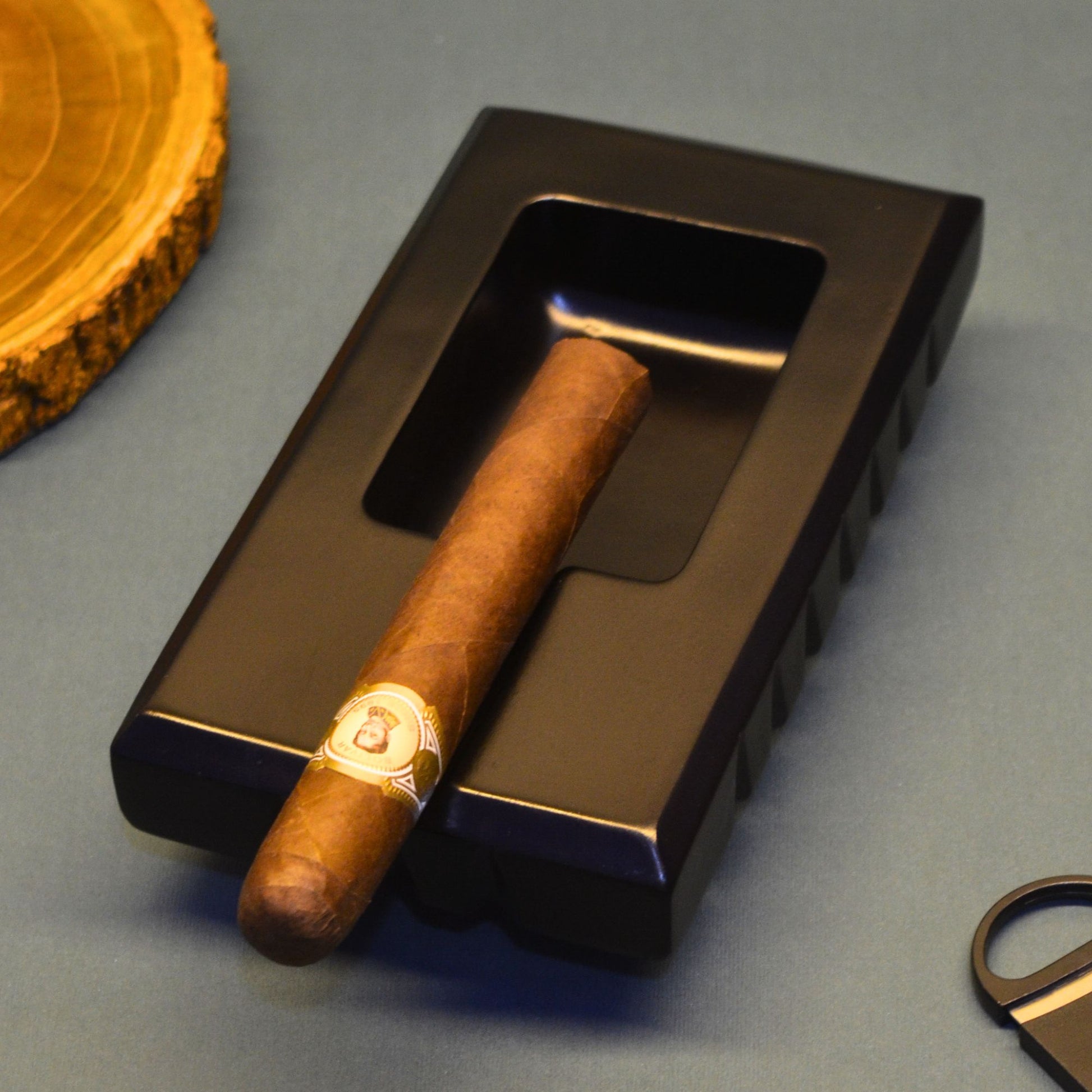 Cigar ashtray on a black metal tray with a wooden coaster in the background