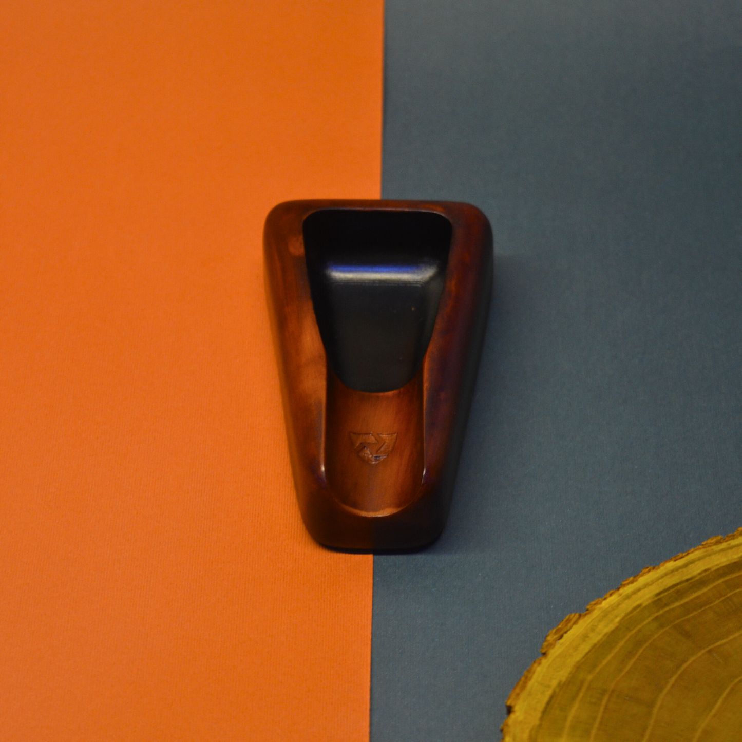 Wooden ashtray with black interior on an orange and blue background