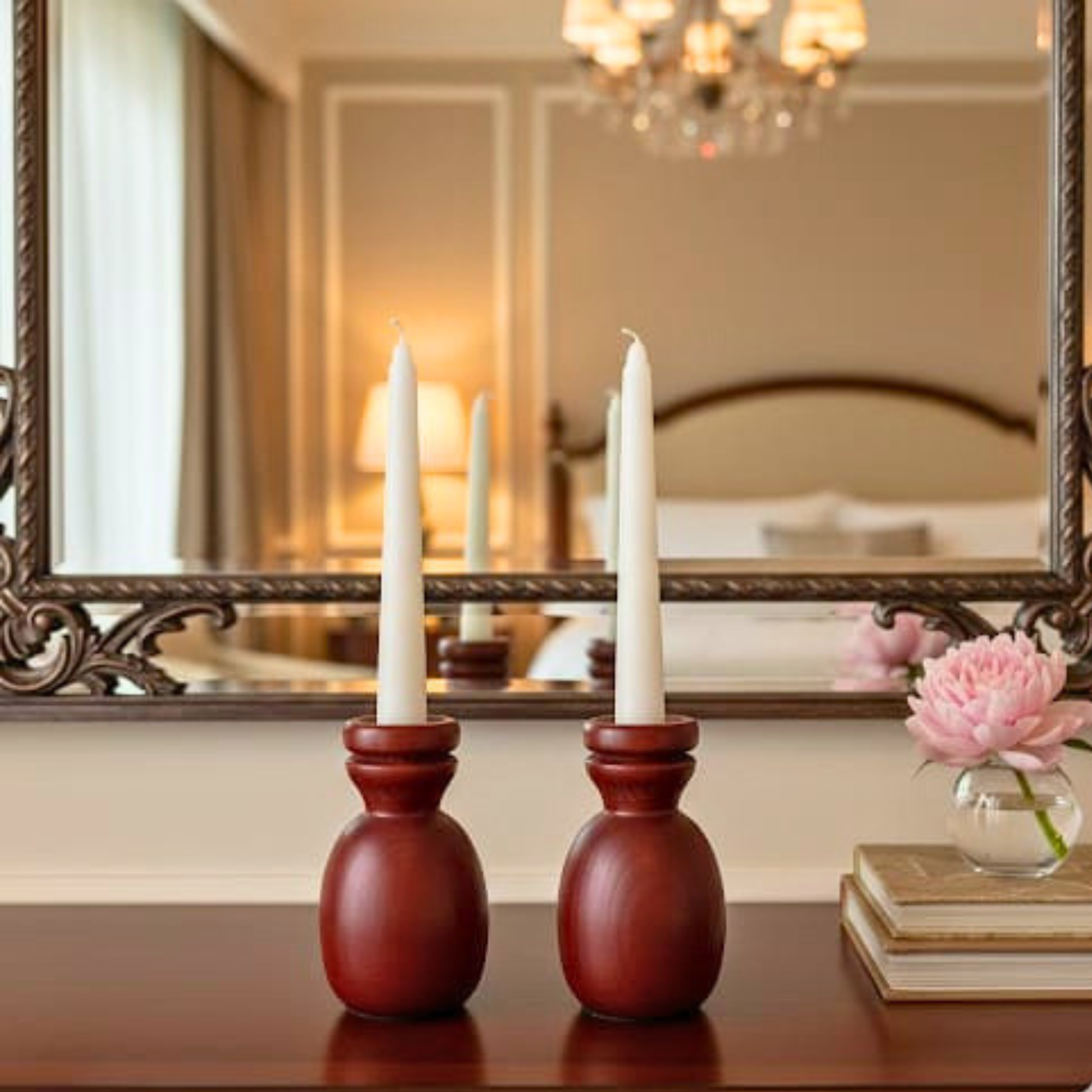 Two red candle holders with white candles on a table in front of a mirror.