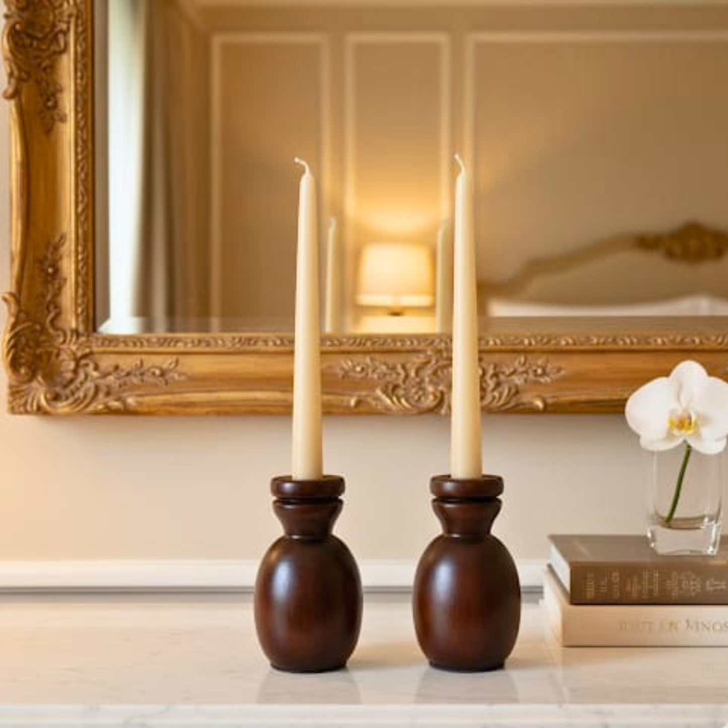 Two wooden candle holders with lit candles on a surface in front of a decorative mirror.