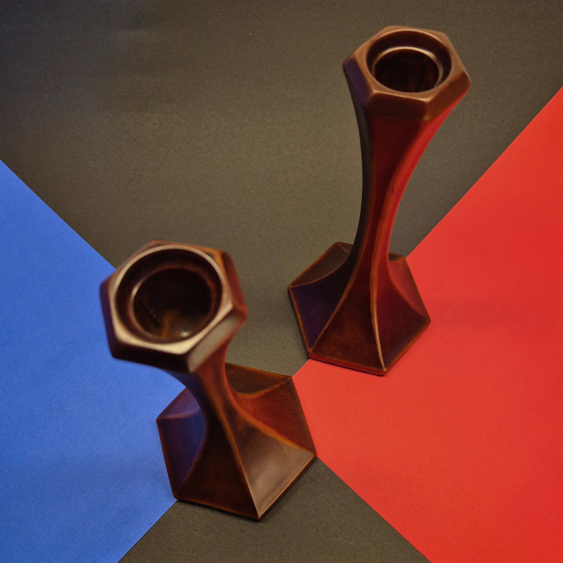 Two brown geometric candle holders on a multicolored background