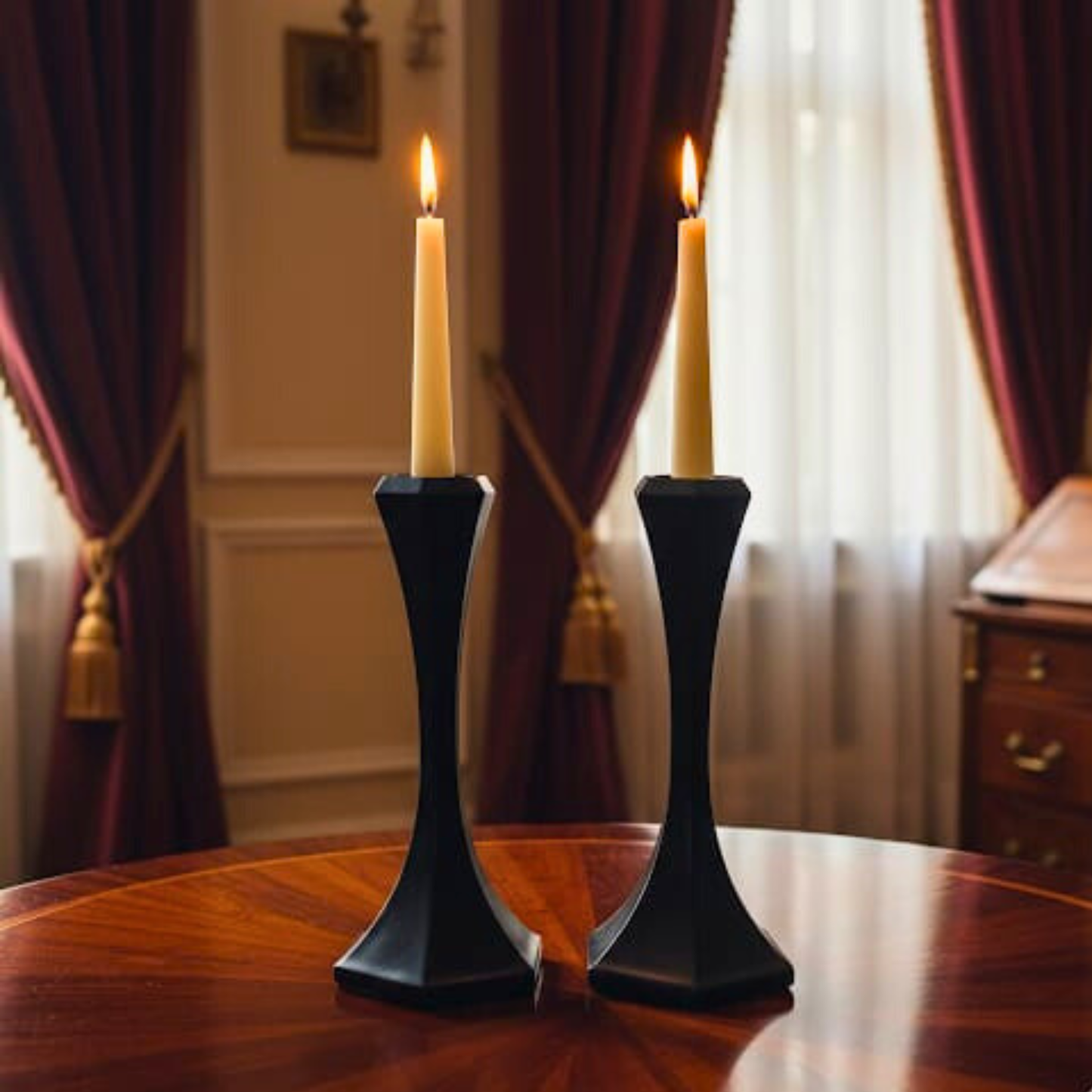 Two black candle holders with lit candles on a wooden table in a room with curtains.