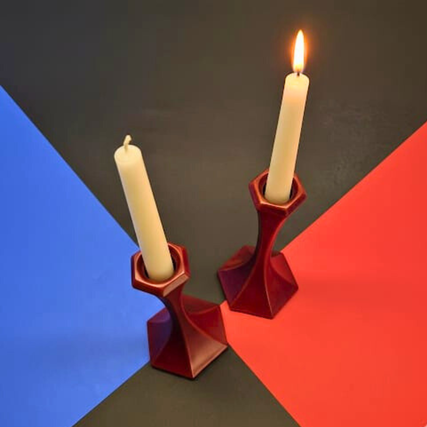 Two red candle holders with lit candles on a black, blue, and red geometric background.