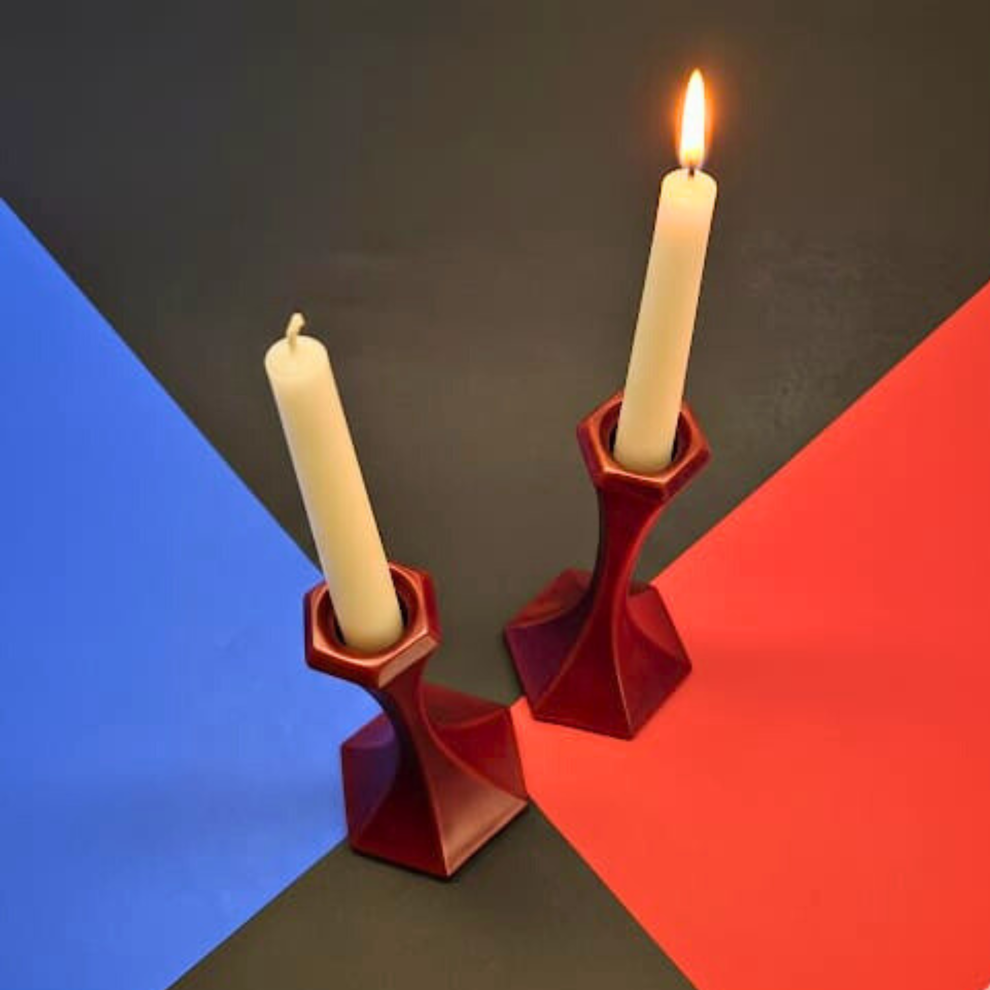 Two red candle holders with lit candles on a black, blue, and red geometric background.